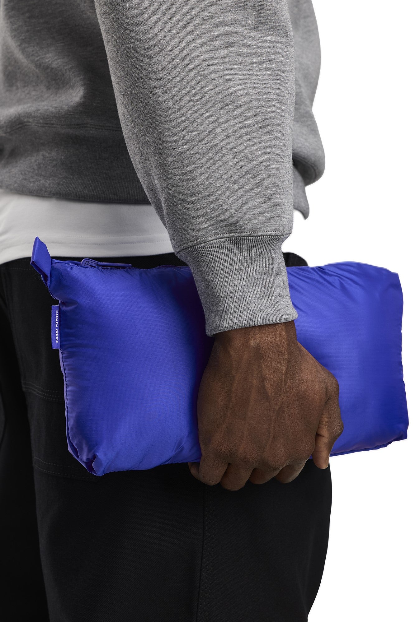 Man in gray sweatshirt holding blue packed jacket.