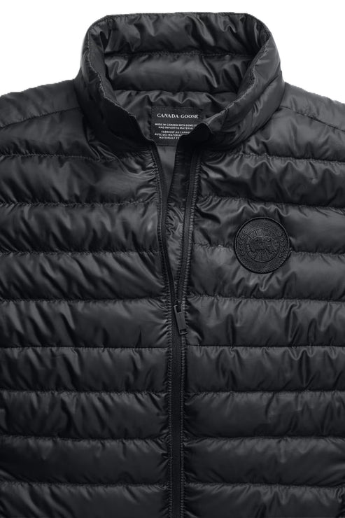 Close-up of a black puffer vest with a black zipper and a round logo on the chest.