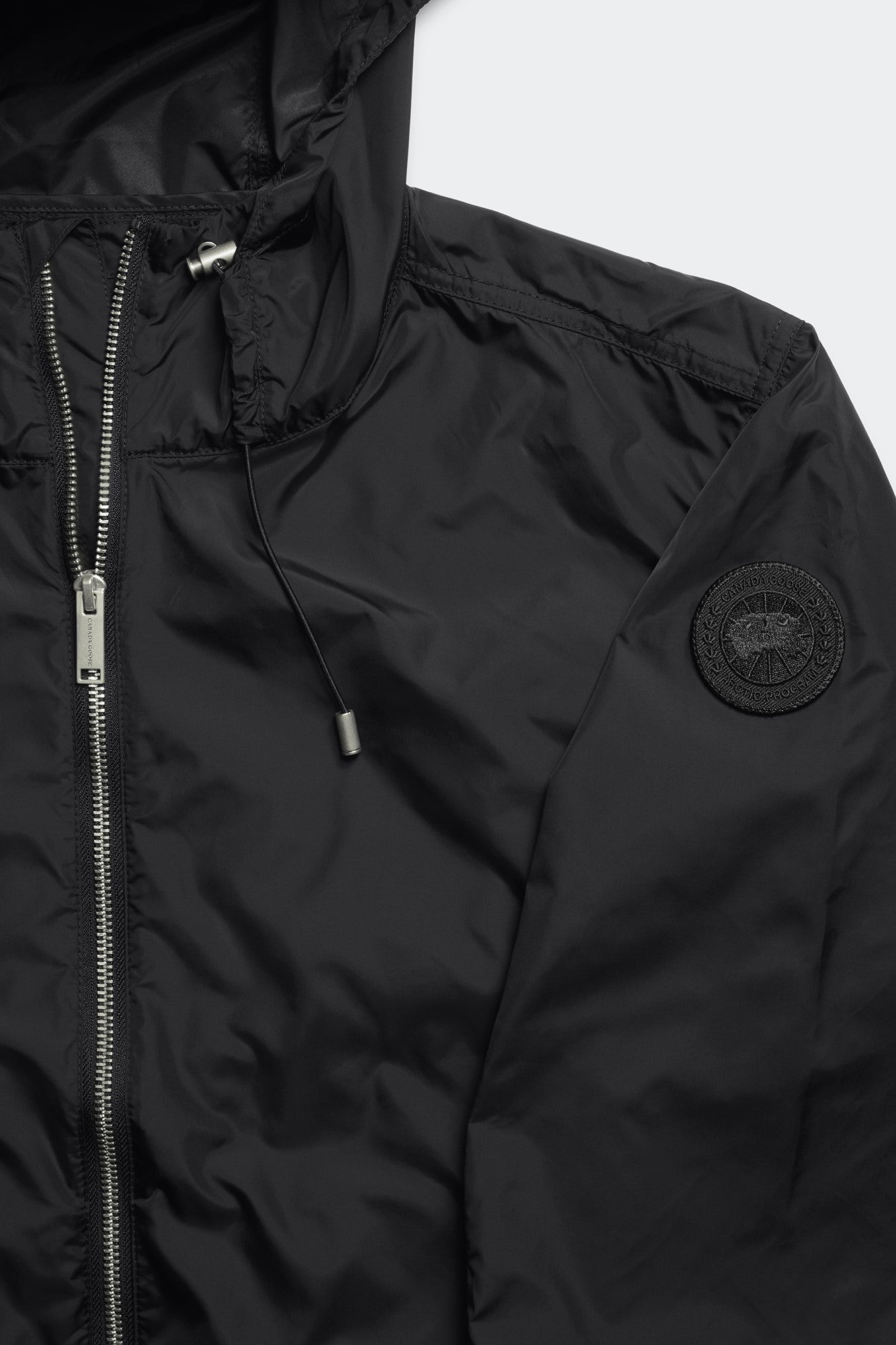 Close-up of a black hooded jacket with a zipper closure, drawstring, and circular patch on the sleeve.