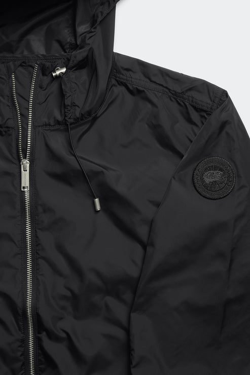 Close-up of a black hooded jacket with a zipper closure, drawstring, and circular patch on the sleeve.