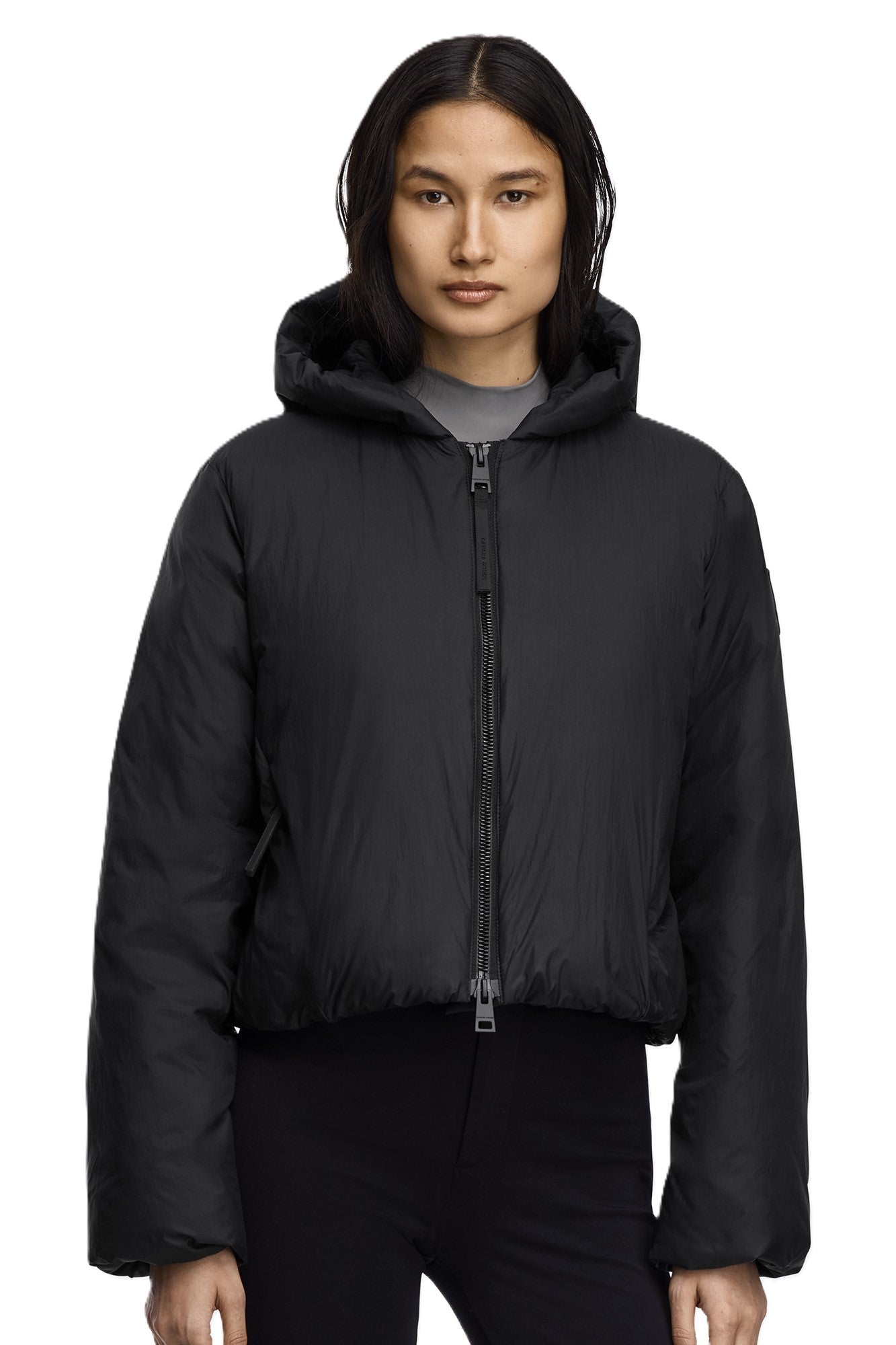 A woman wearing a black, hooded, cropped puffer jacket with a zipper.