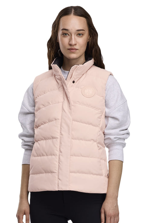 A person wearing a light pink puffer vest with a snap closure, and a subtle circular logo on the chest.