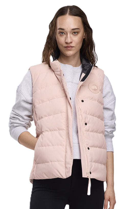 A woman wearing a light pink, quilted vest with black buttons and a white string. She wears a light grey sweatshirt under the vest.