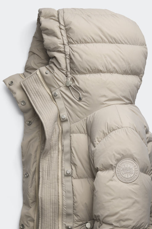 A close-up of a beige down jacket with a large hood and a circular emblem on the sleeve.