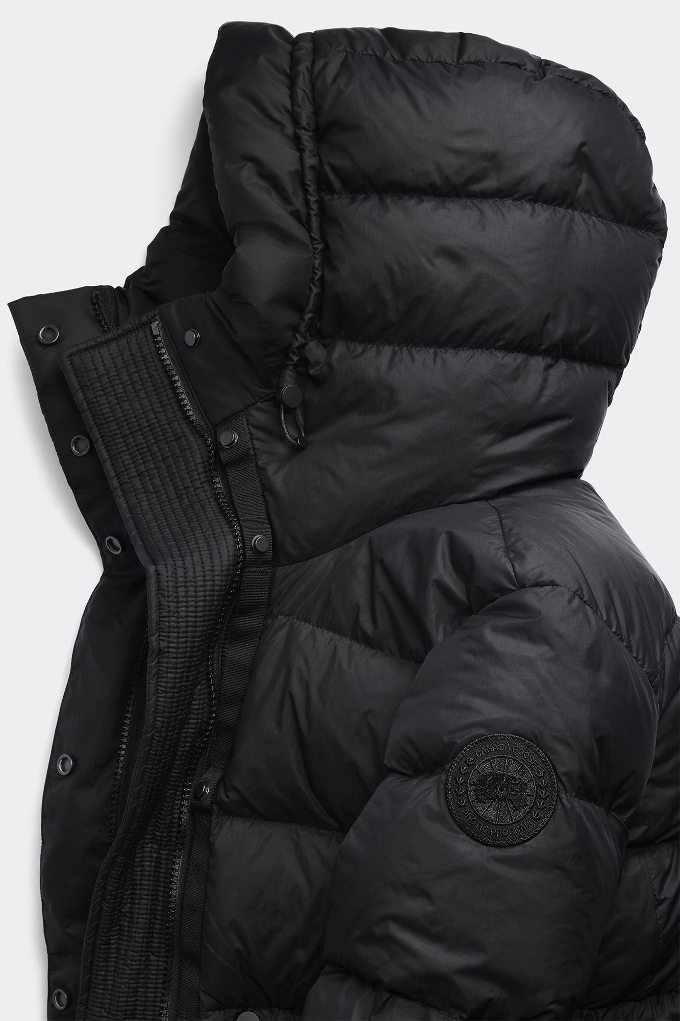 Close-up of a black puffer jacket featuring a hood and a circular logo patch.