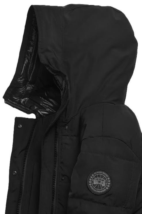 A close-up view of a black, hooded winter parka, highlighting the quilted texture, a prominent black, circular Arctic Program logo patch on the left sleeve, and the front zipper closure with snap buttons.
