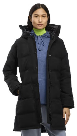 A woman wearing a long-sleeved, knee-length black hooded puffer coat over a blue hoodie with a light green mock-neck collar visible underneath.
