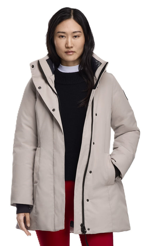 A woman wearing a hip-length, light beige parka with a black collar and black closures.