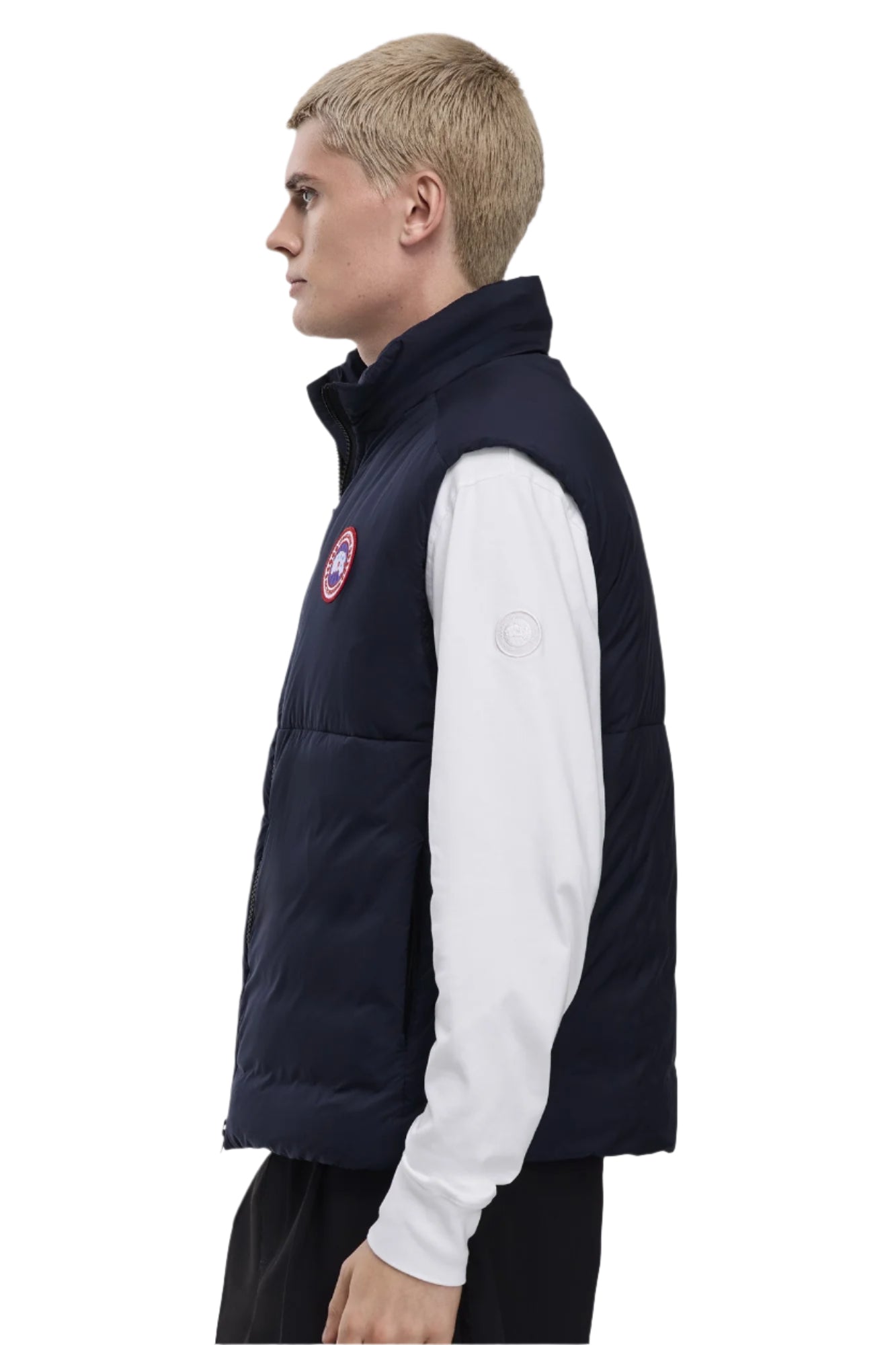 A side view of a person wearing a navy blue quilted vest with a circular badge on the chest.