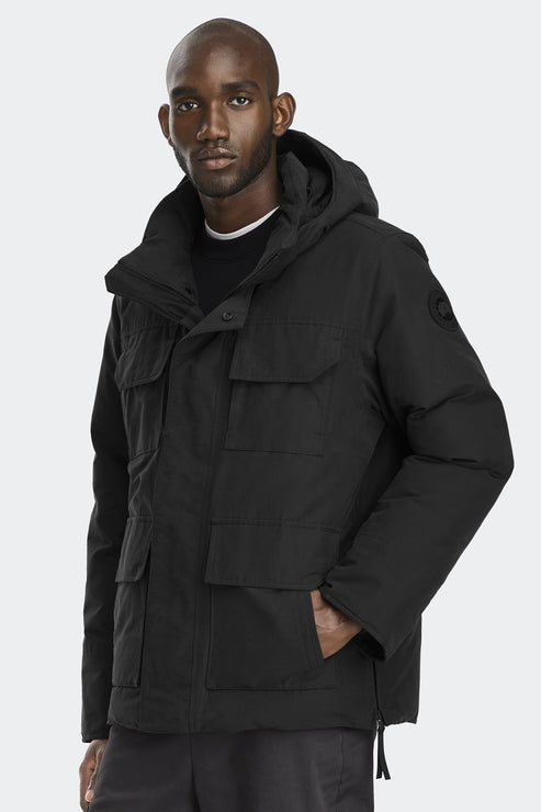 A Black man wears a black hooded parka jacket with multiple flap pockets.