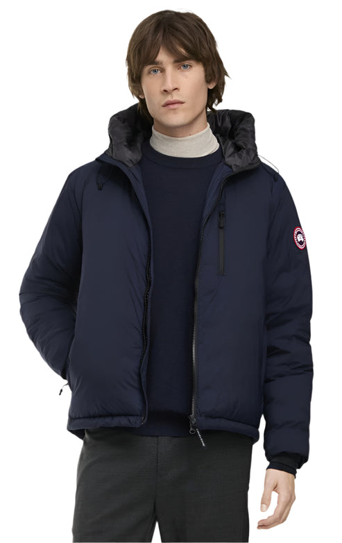 A man wearing a navy blue winter coat with a hood, a turtleneck, and black pants.