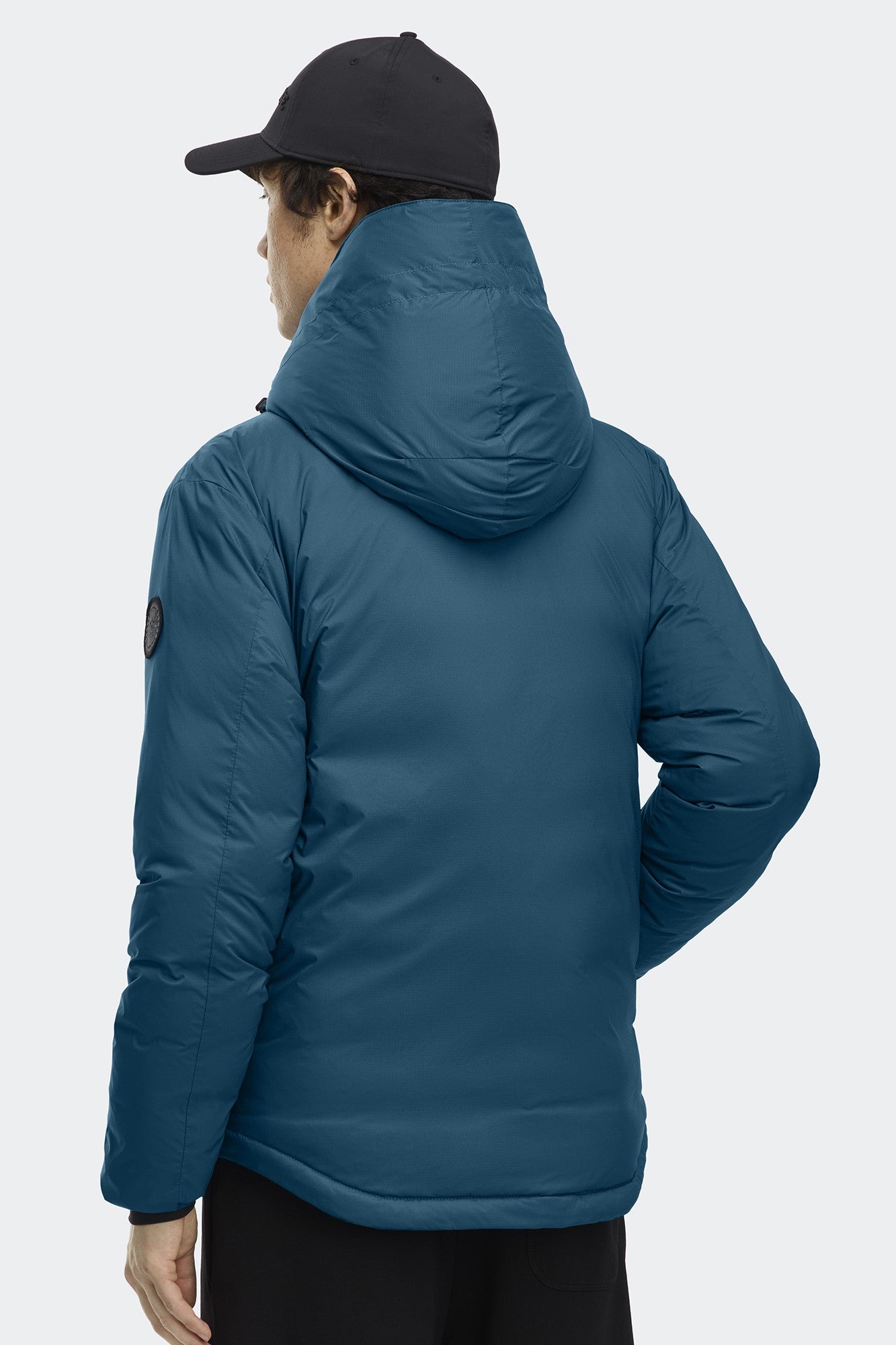 Blue puffer jacket with hood and black baseball cap worn by a person facing away from the viewer.