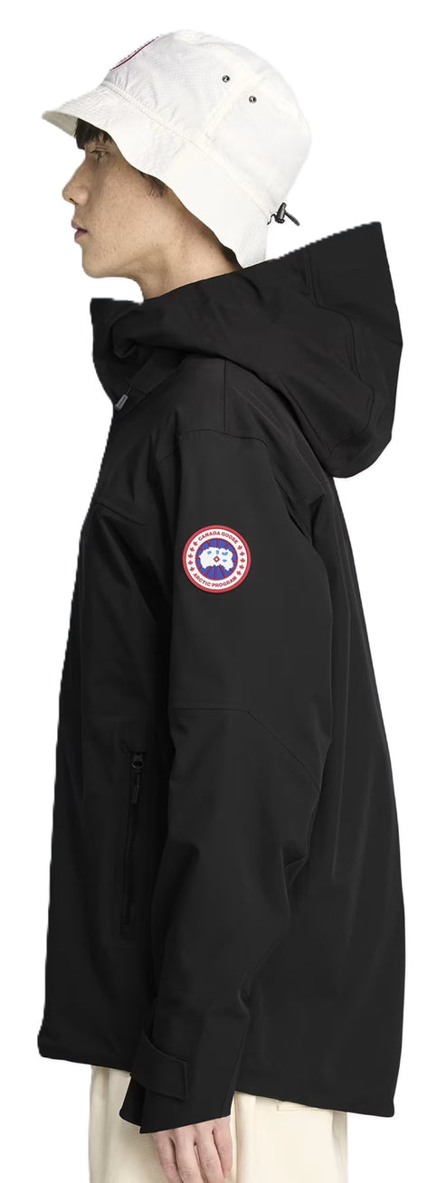 A person wears a white hat and a black hooded jacket with a round logo patch on the sleeve.