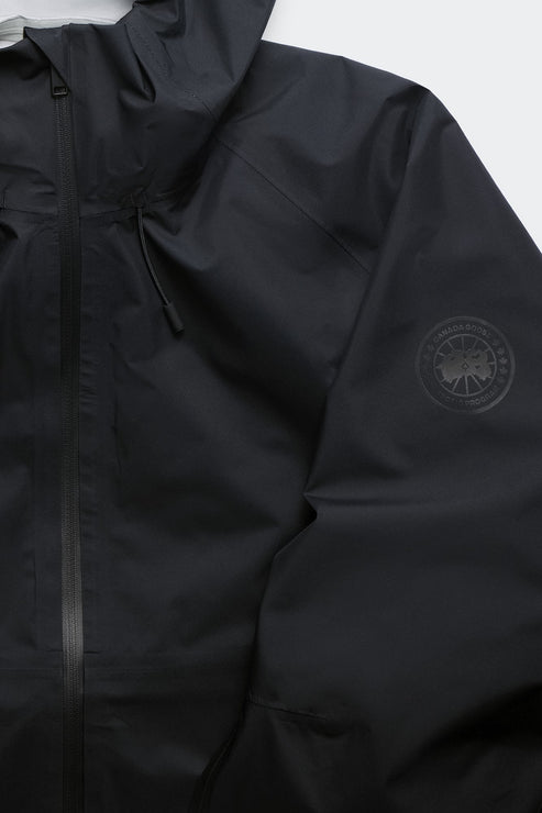 Close-up of a black hooded rain jacket with a circular logo on the sleeve and a vertical zipper.