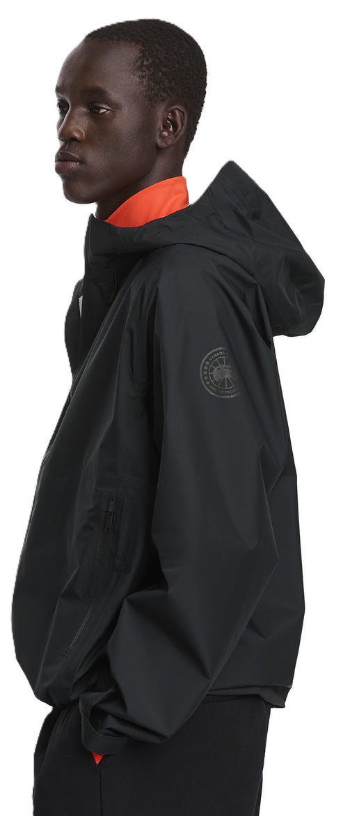 A person wears a black hooded jacket with an orange collar.