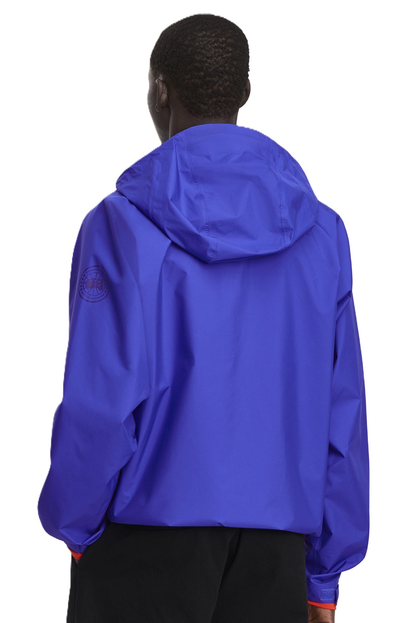 A person is facing away wearing a hooded purple lightweight jacket with raglan sleeves and black pants.