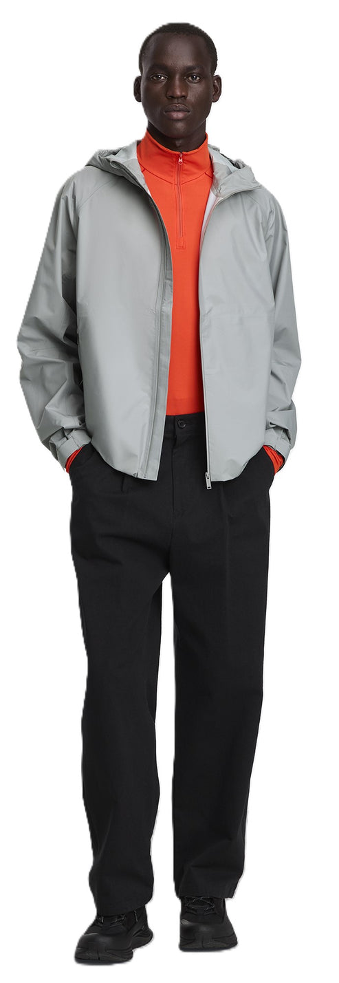A Black male model wearing an orange turtleneck top, light gray jacket, and black pants and shoes.