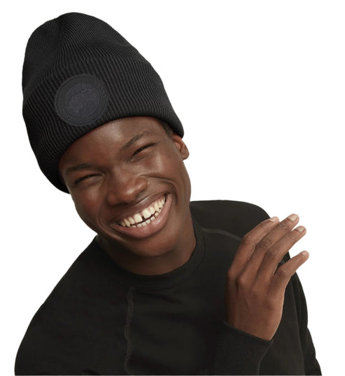 Person wearing a black knit beanie with a circular logo.