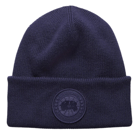 Close-up of navy blue knit beanie with circular patch on front.