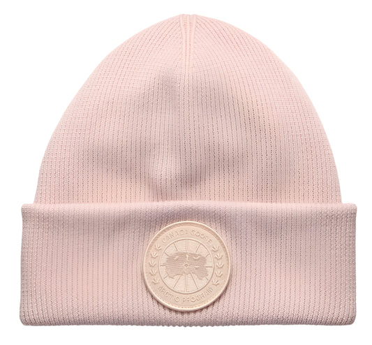 Light pink knit beanie with circular emblem on the brim.