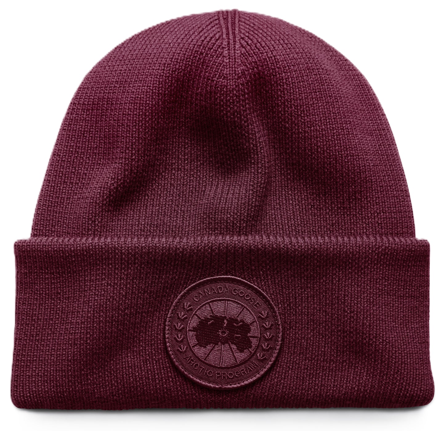 A deep burgundy ribbed knit beanie with a folded cuff featuring a circular tonal logo patch embroidered with text reading CANADA GOOSE ARCTIC PROGRAM.
