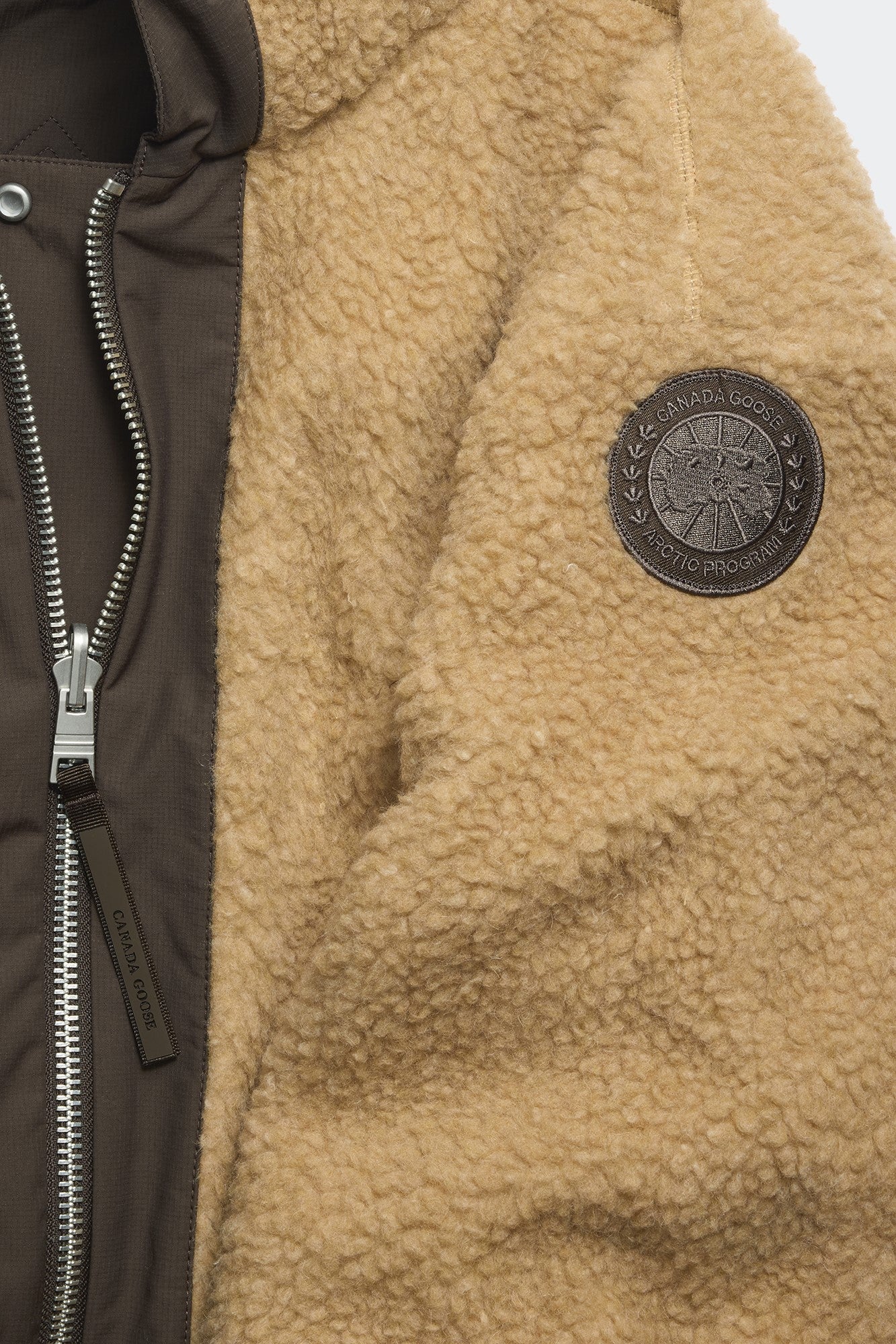 Close up of brown and beige jacket with visible zipper and brand emblem.