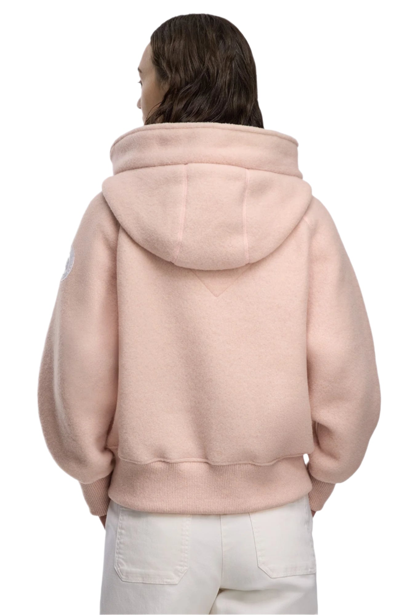 Rear view of a light pink hoodie with a large hood and ribbed hem on a person.