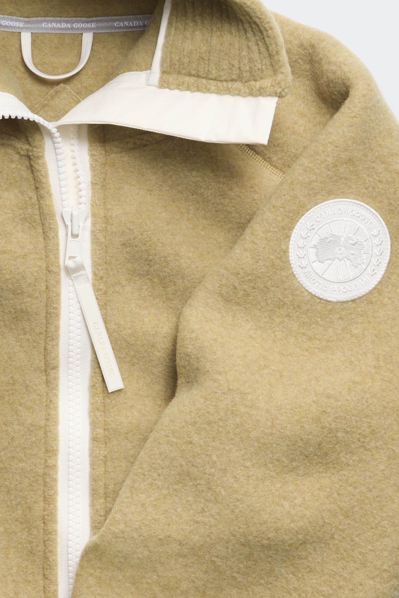 Tan fleece jacket with white zipper and collar, and a white circular logo patch on the sleeve.