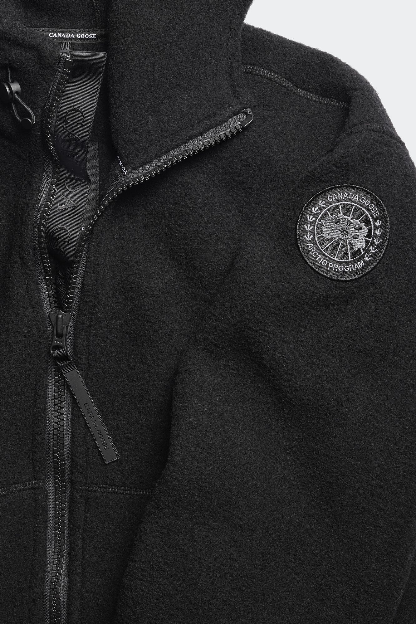 Close-up of a black fleece jacket with a zipper, collar, and circular logo on the right chest.