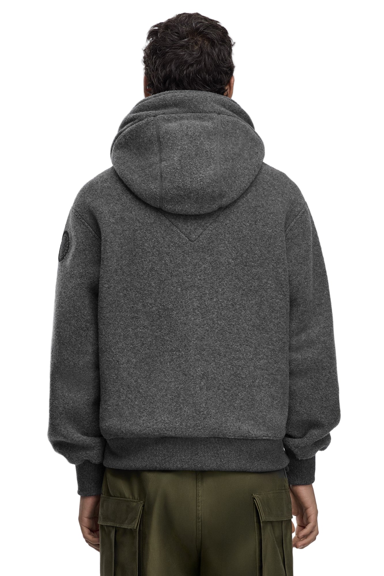 A gray, wool-blend hooded sweatshirt with a circular logo on the left shoulder and a kangaroo pocket worn with olive-green cargo pants, rear view.