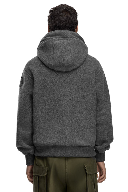 A gray, wool-blend hooded sweatshirt with a circular logo on the left shoulder and a kangaroo pocket worn with olive-green cargo pants, rear view.