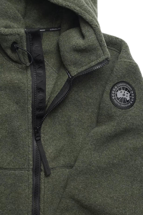 Close-up of a green hooded jacket with black zipper, drawstrings, and circular logo patch featuring a compass design.