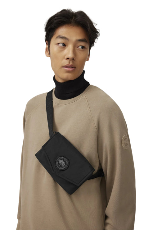 Person wearing a tan sweater and black turtle neck with a black messenger bag over the shoulder.