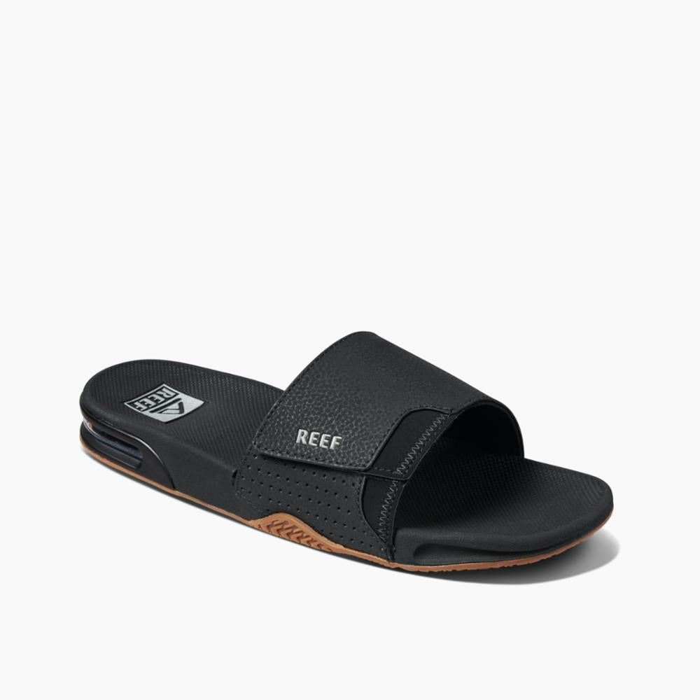 Black slide sandal with a padded strap that says REEF.