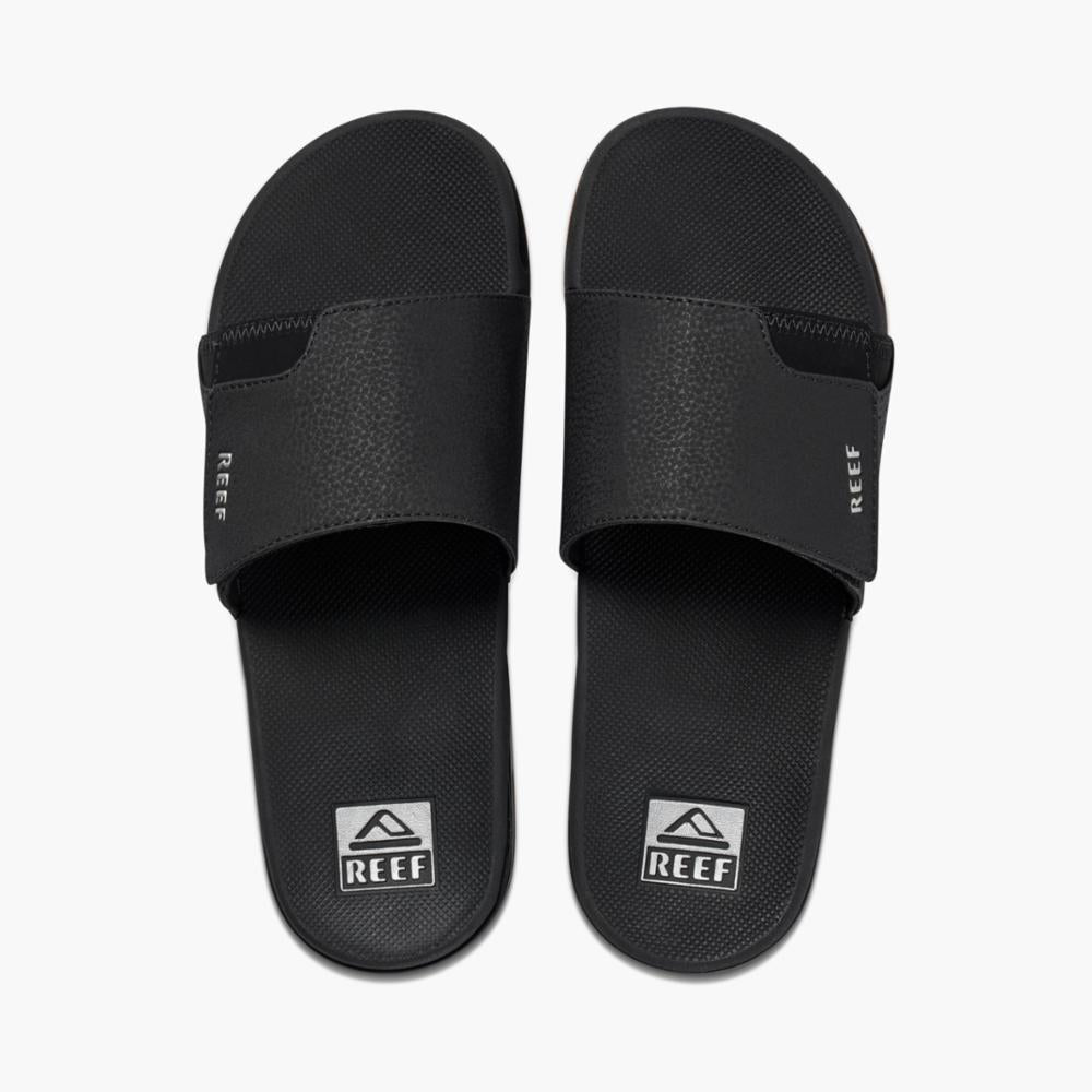 Pair of black slide sandals, each with a REEF logo at the toe.