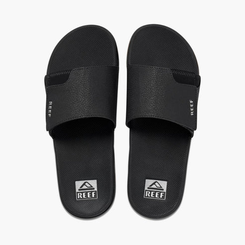 Pair of black slide sandals, each with a REEF logo at the toe.