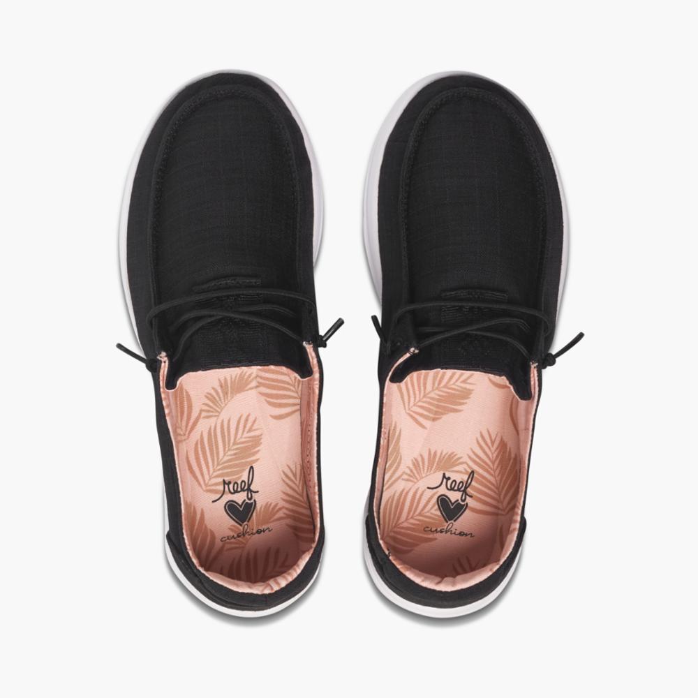 Top-down view of black slip-on shoes with white soles and peach leaf patterned insoles.