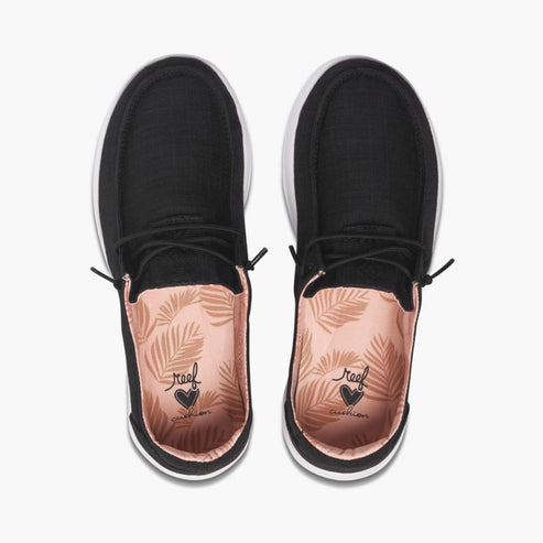 Top-down view of black slip-on shoes with white soles and peach leaf patterned insoles.