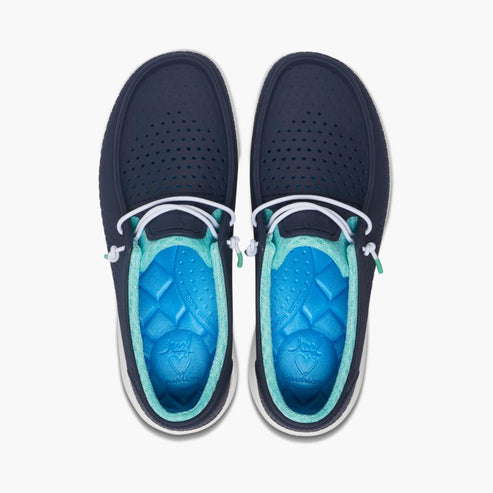 Overhead view of navy blue slip-on shoes with decorative white laces and blue molded insoles with teal trim.