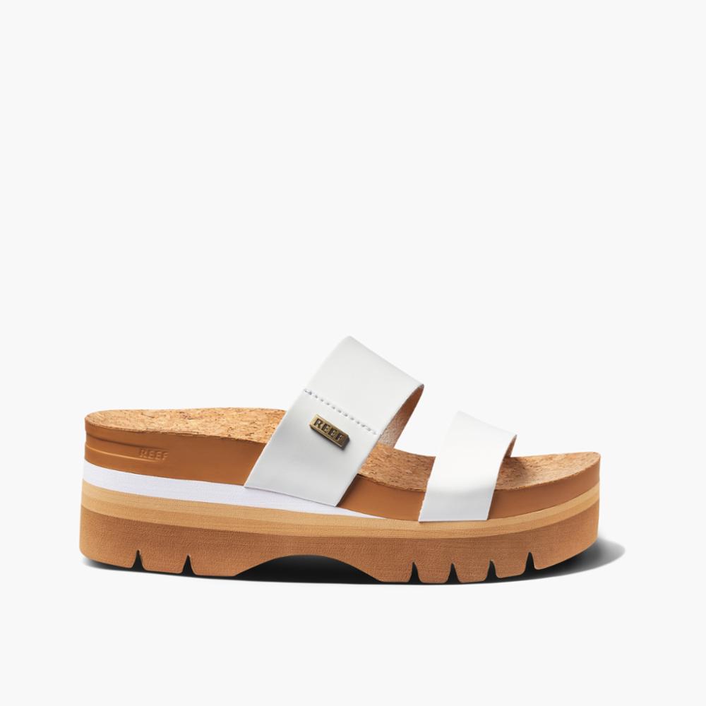 A women's platform slide with white straps, a cork footbed, and a brown lug sole.