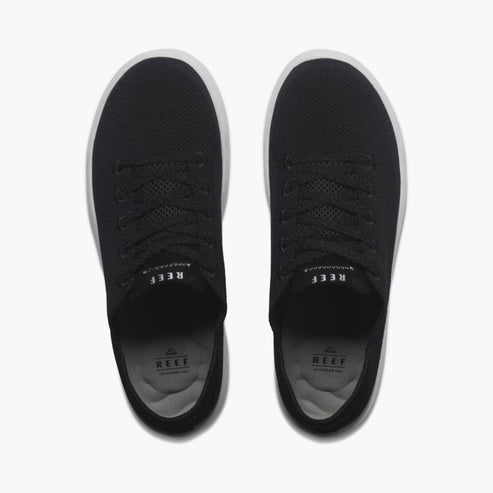 A pair of black sneakers with white soles, seen from above, showing shoelaces and brand labels on the inner sole.