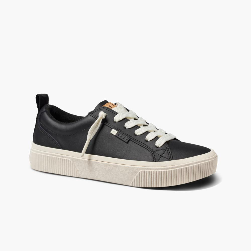 Black low-top sneaker with white laces and a tan tongue tag.