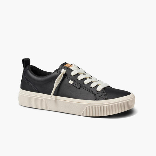 Black low-top sneaker with white laces and a tan tongue tag.