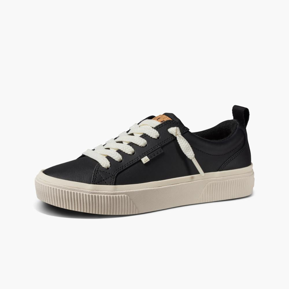 Black sneaker with white laces and thick tan rubber sole.