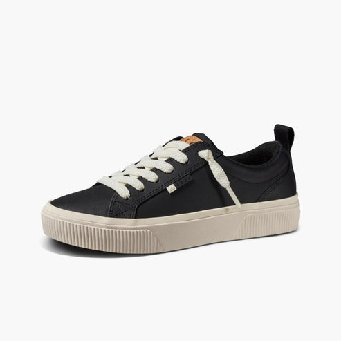 Black sneaker with white laces and thick tan rubber sole.
