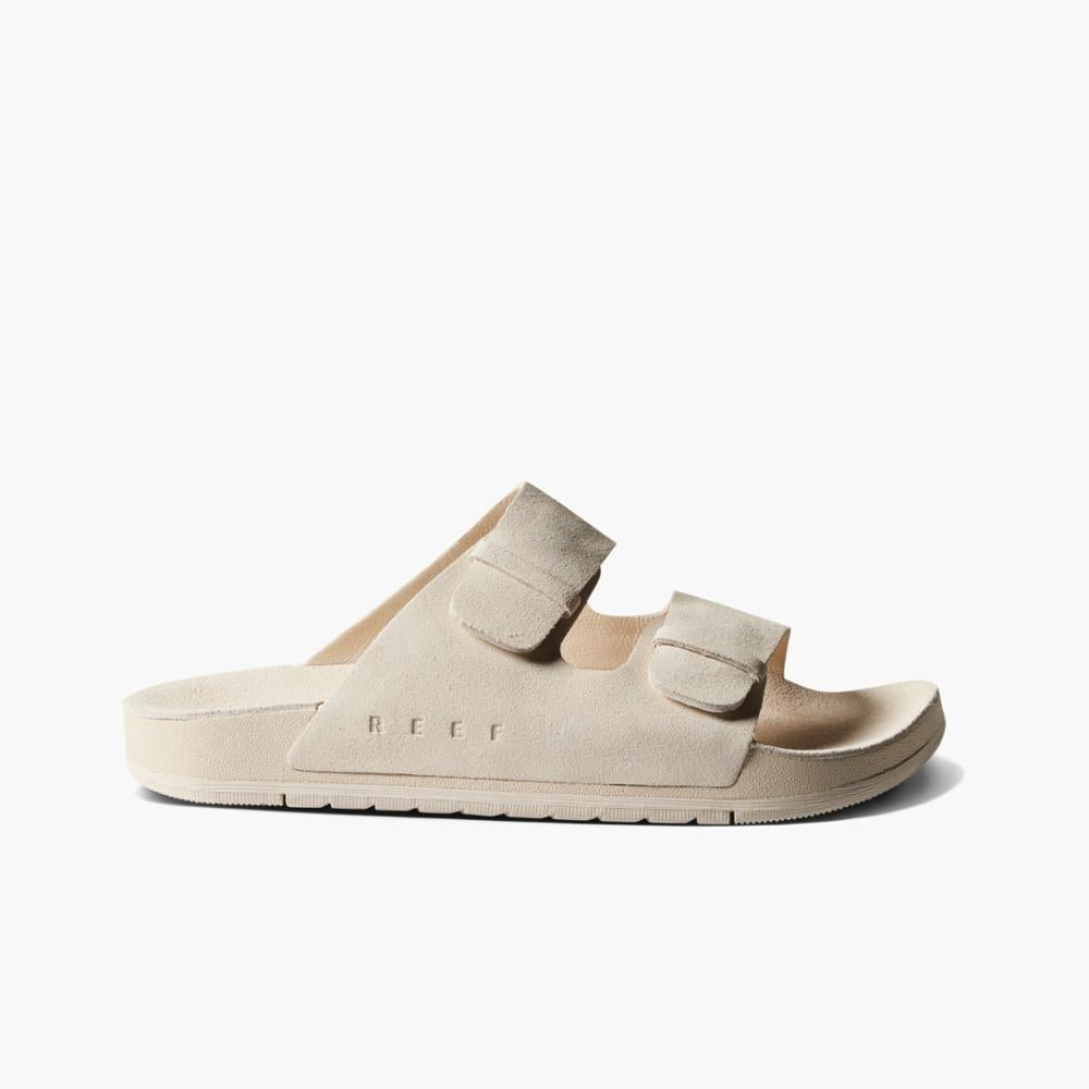 Beige slide sandal with two adjustable hook and loop straps and the word REEF in small letters on the side.