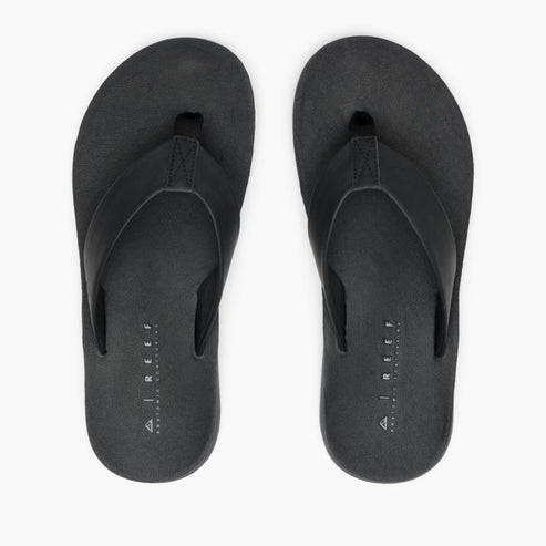 Two black flip-flops with fabric toe posts and “REEF” text visible on the insole.