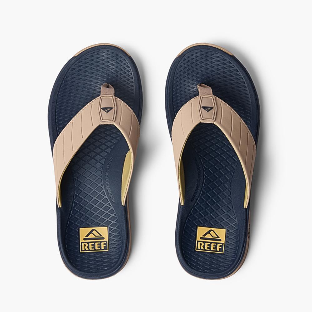 Pair of navy blue flip-flops with beige straps and a textured footbed, displaying the word "REEF" on a yellow rectangle near the heel.