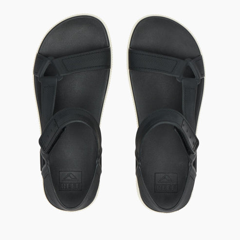 Overhead view of a pair of sandals: Black footbed and straps with an embossed square logo near the heel.