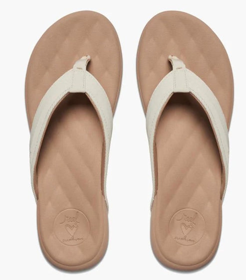 A pair of beige flip-flops with off-white straps viewed from directly above, featuring a textured footbed with a small stamped heart logo.